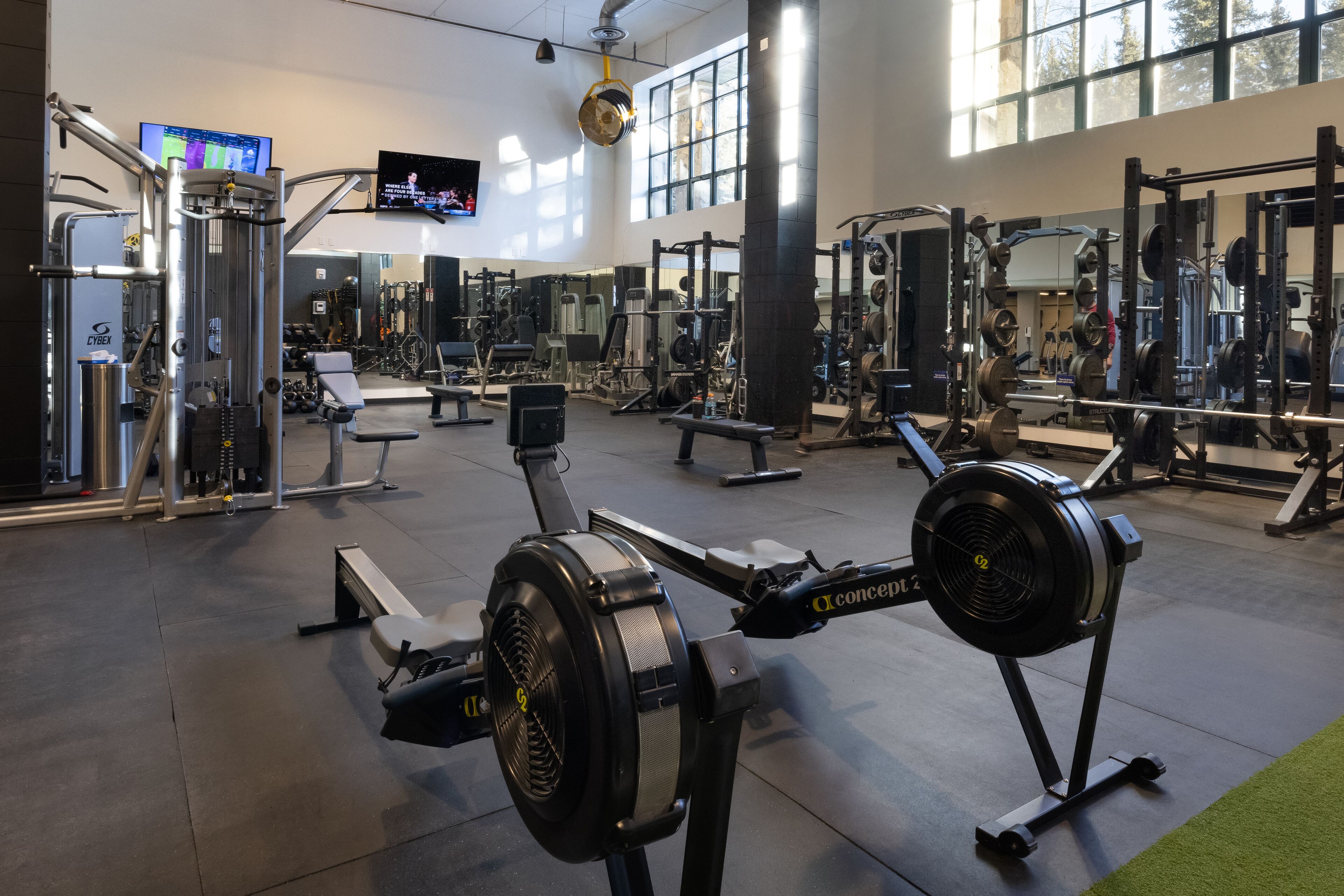 A gym with various exercise equipment, a television screen, and large windows.