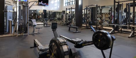 Ein Fitnessstudio mit unterschiedlichen Trainingsgeräten, einem Fernsehbildschirm und großen Fenstern.