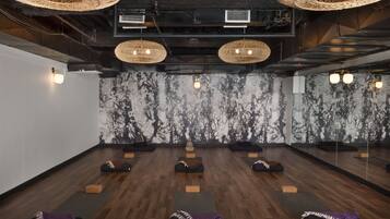 A room with wooden floors, black mats, and a marble wall with a tree pattern. There are ceiling lights and a large mirror.
