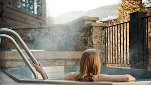 Une personne se détend dans un bain à remous, avec un mur de pierres et une rambarde en métal en arrière-plan.