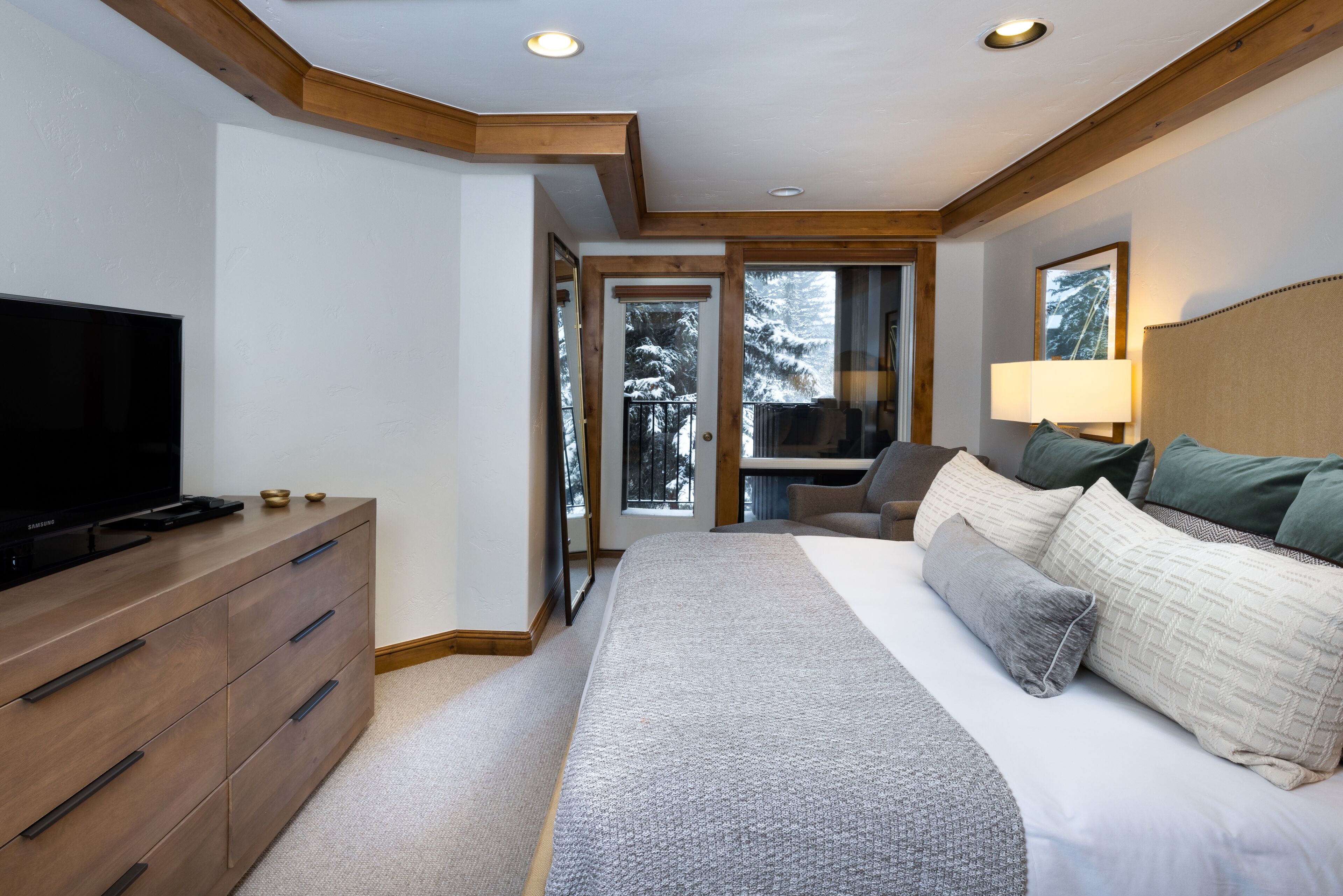 Une chambre à coucher avec un lit, une télévision, une commode et une fenêtre donnant sur des arbres.