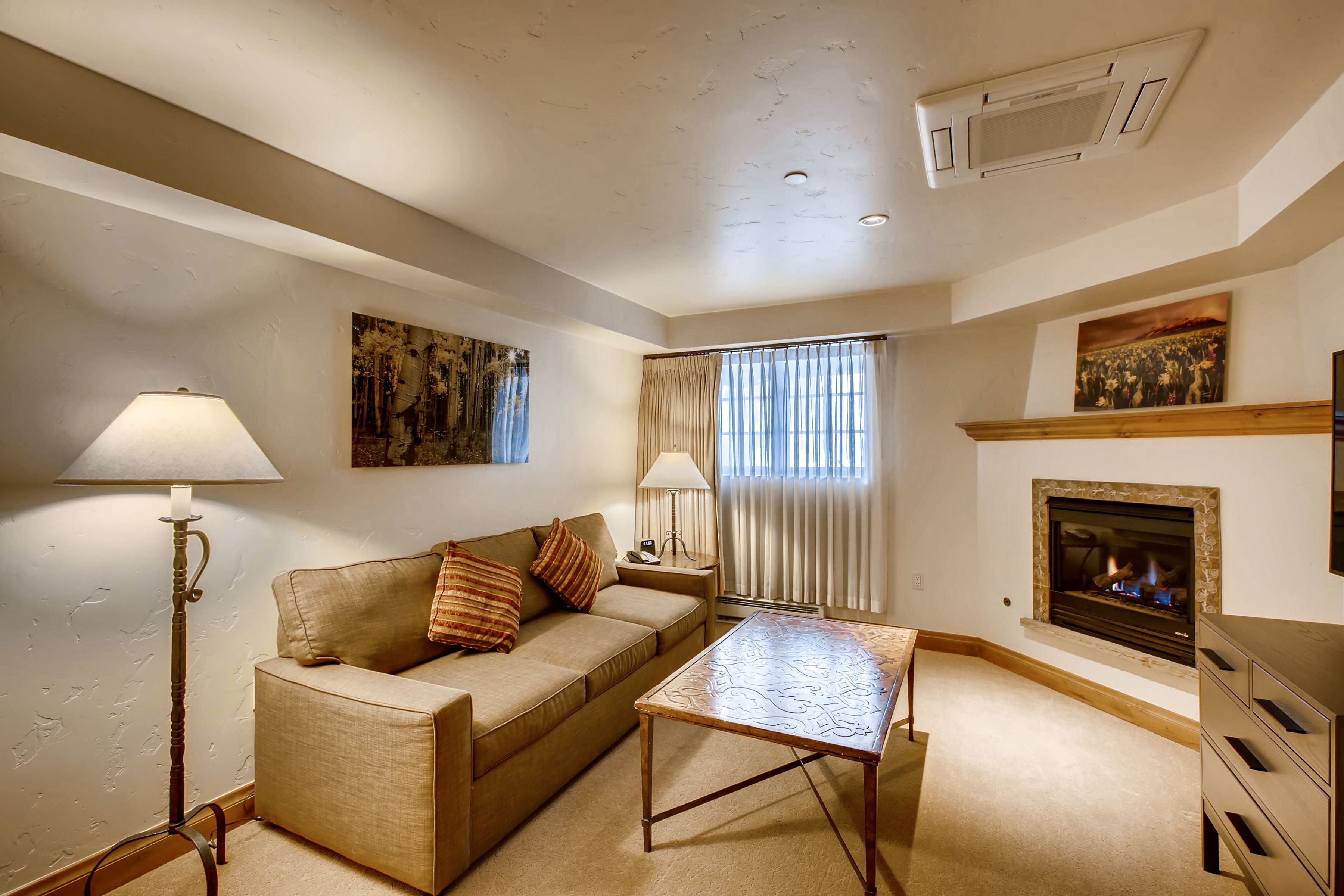 A living room with a sofa, two lamps, a fireplace, and a painting on the wall.