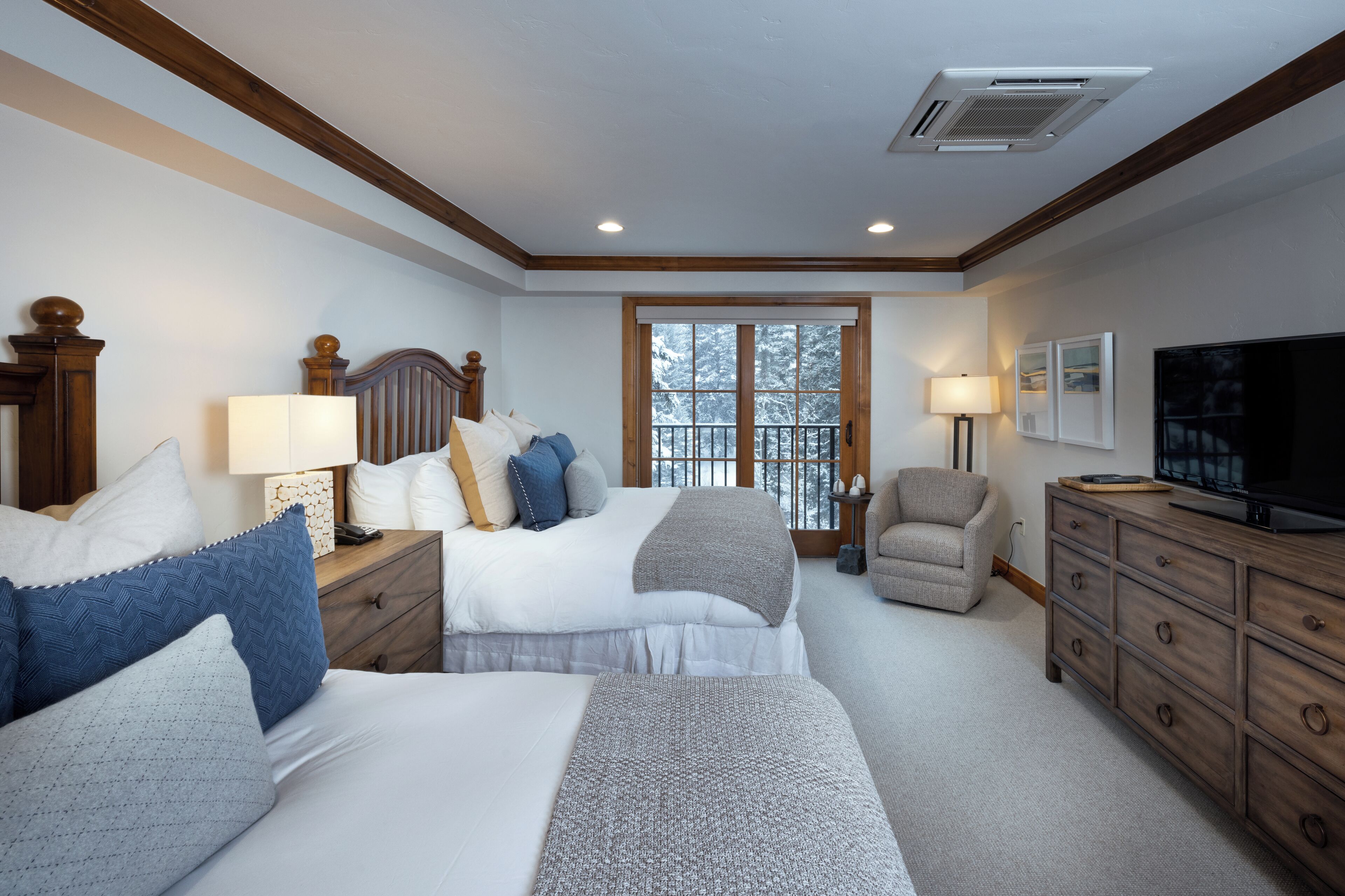 A hotel room with two beds, a TV, a desk with a lamp, a chair, and a large window.