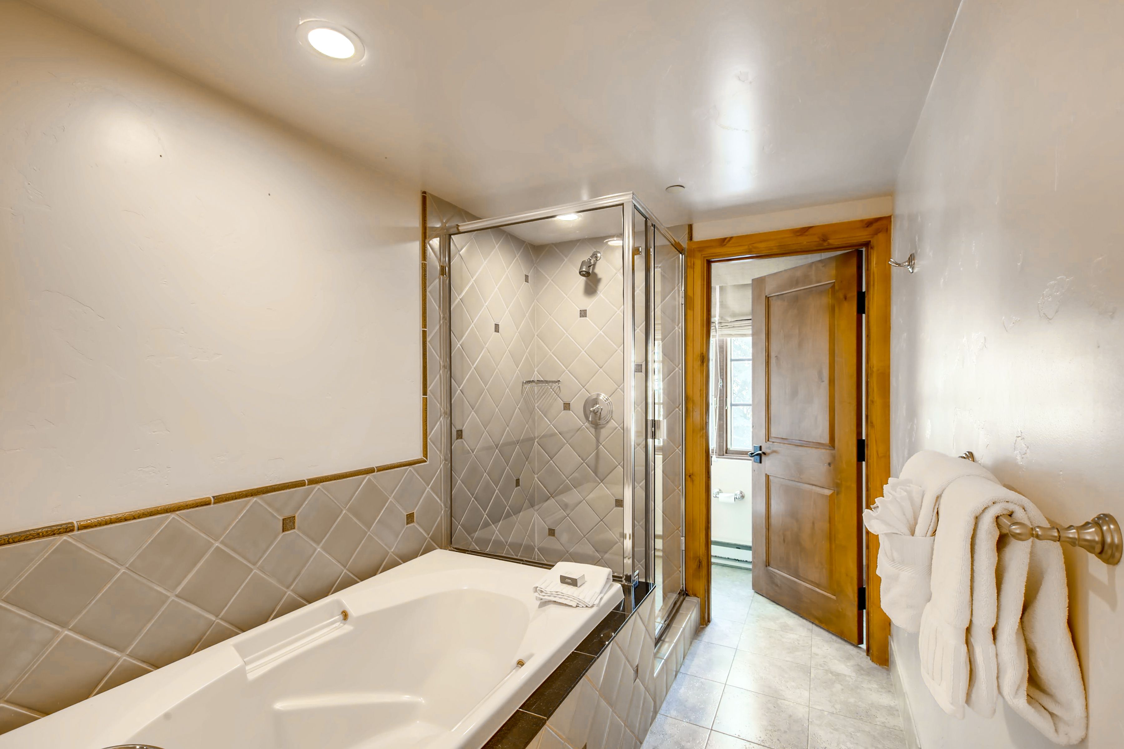 A modern bathroom with a large bathtub, a glass-enclosed shower, and a wooden door leading to another room.