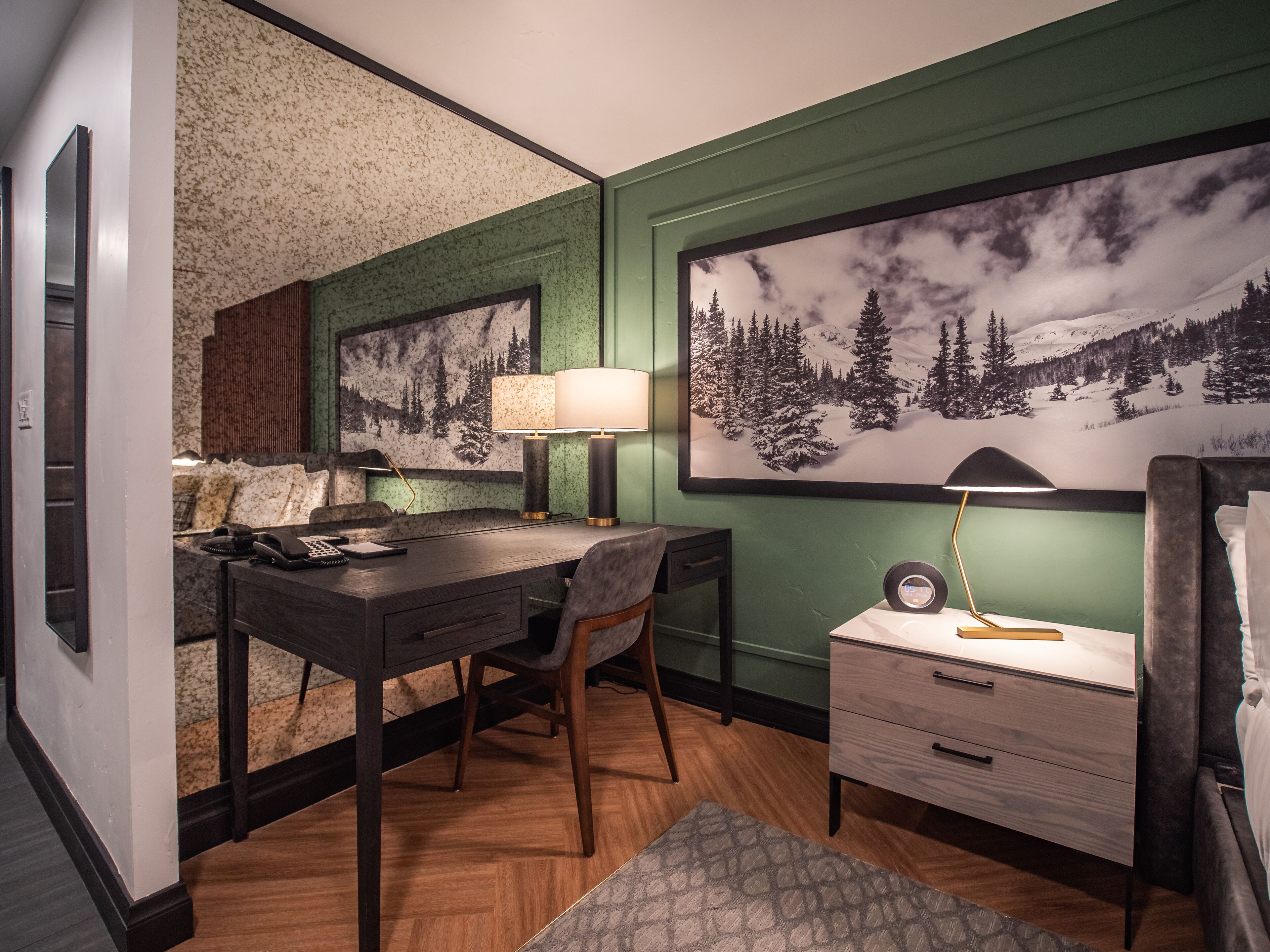 Habitación de hotel con escritorio, silla y una gran foto enmarcada de un paisaje montañoso nevado.