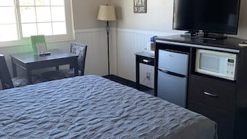 Ett hotellrum med en säng, ett skrivbord med en stol, en tv, en mikrovågsugn och ett kylskåp.