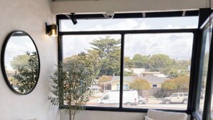 A cozy room with two chairs, a small table, a potted plant, and a view of the outside. - Morro Crest Inn (Morro Bay)