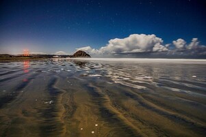 Una playa con cielo despejado, una montaña distante y un puente al fondo.