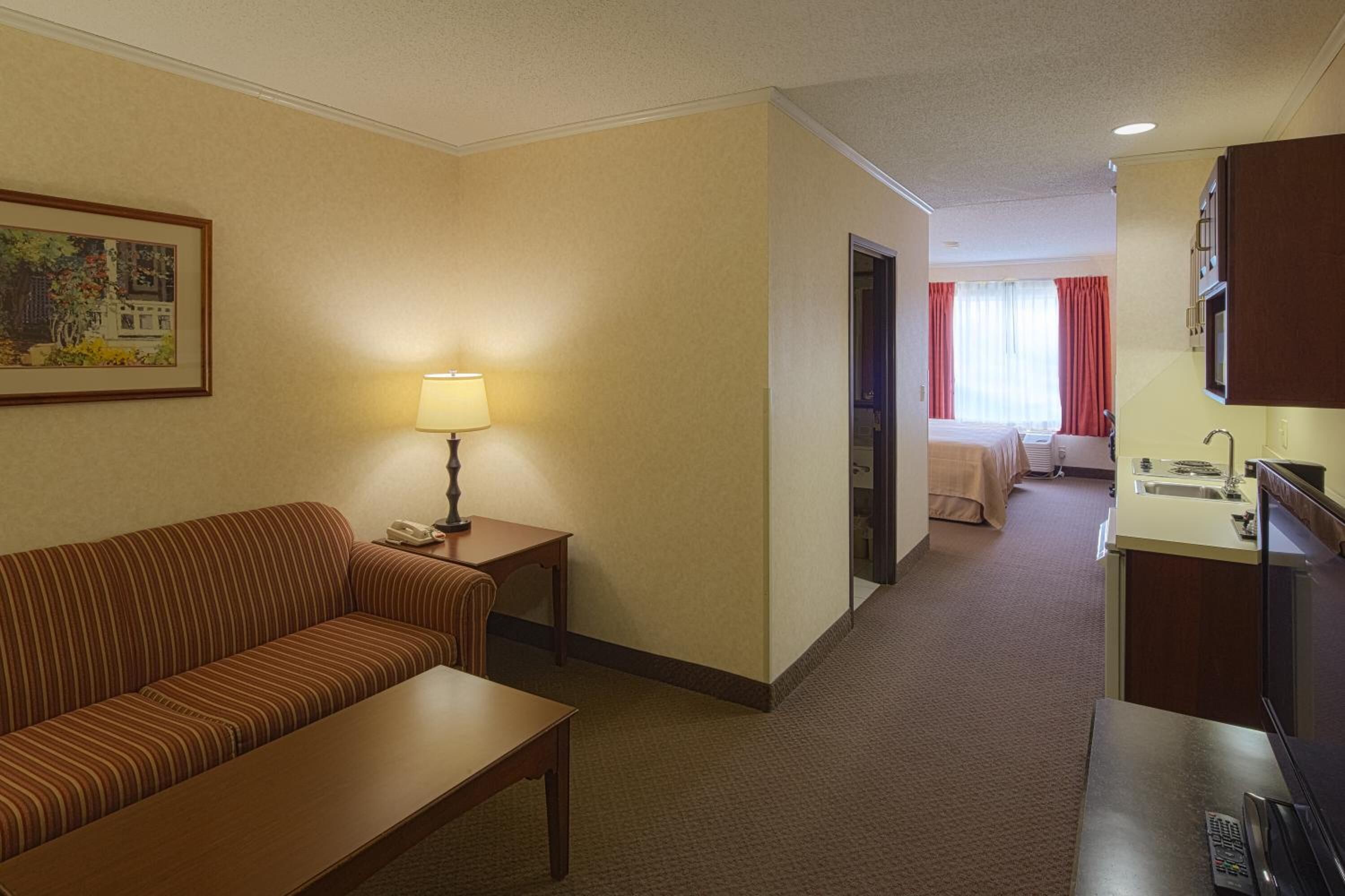 A hotel room with a sofa, a small table, a lamp, a bed, a bathroom, and a TV.