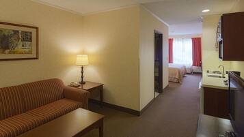 A hotel room with a sofa, a small table, a lamp, a bed, a bathroom, and a TV.
