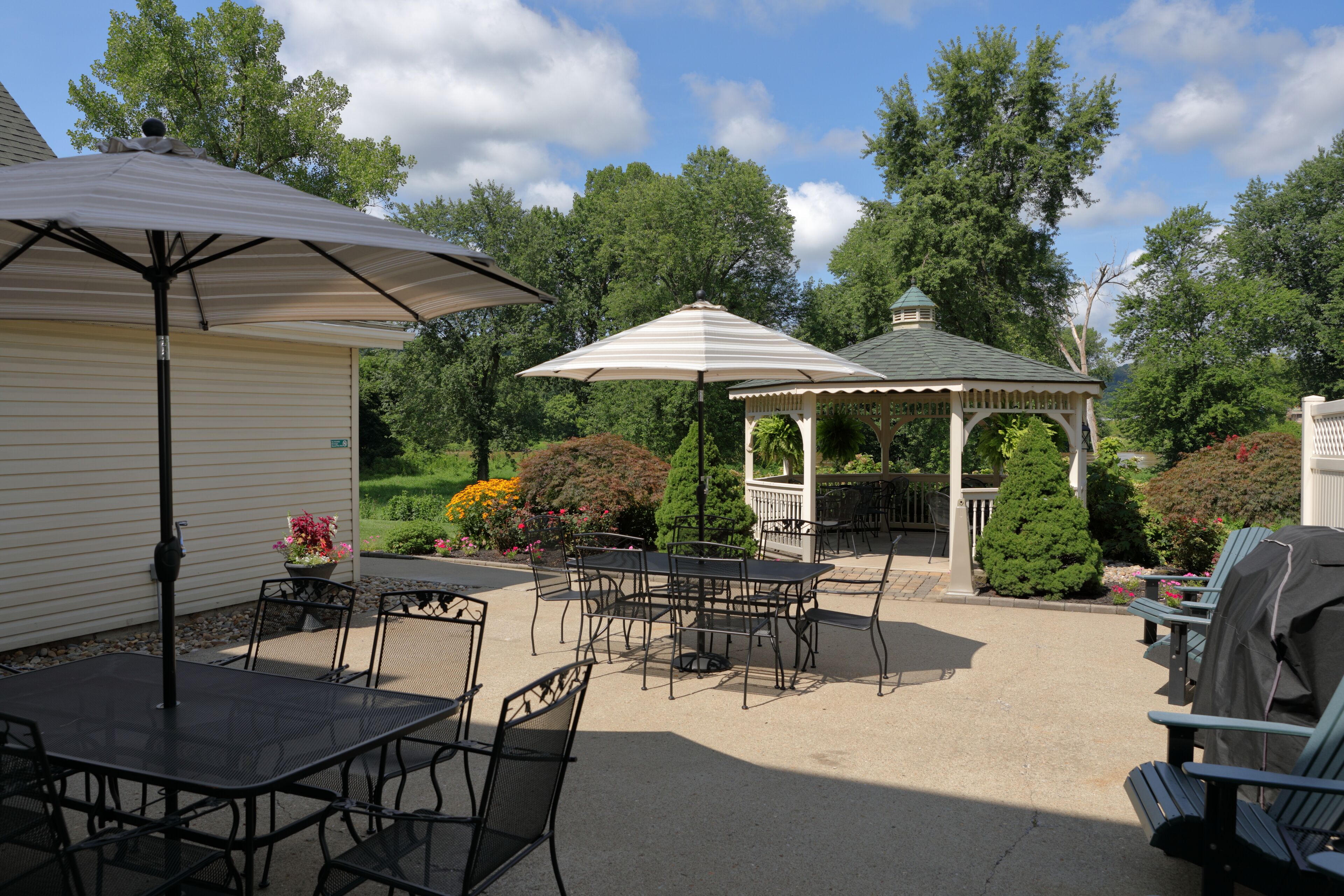 Een terras buiten met tafels, stoelen, een pergola en een barbecue.