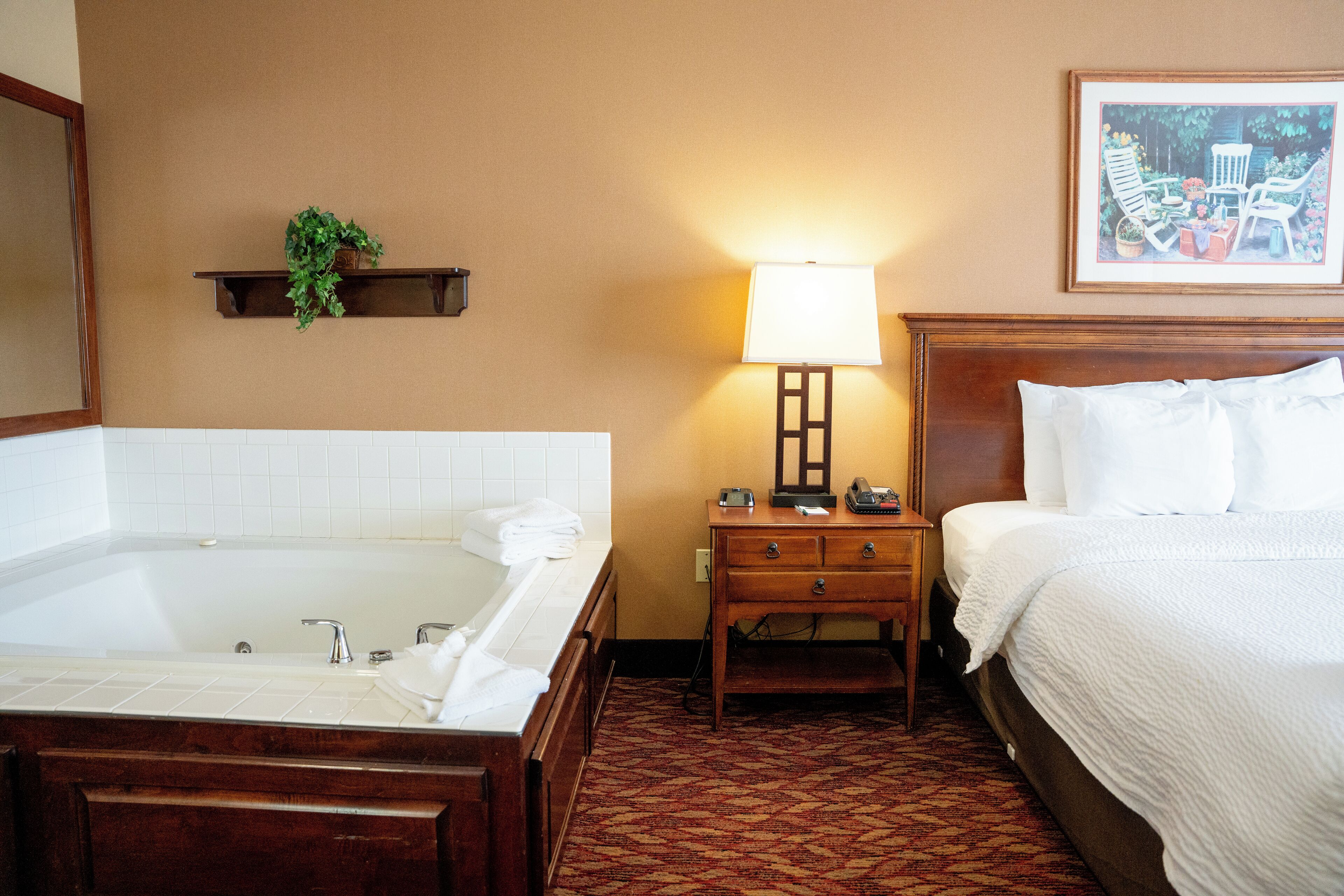 Habitación de hotel con una bañera grande, una mesita de noche con lámpara y una cama con ropa blanca.