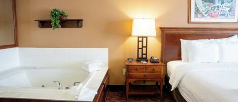Habitación de hotel con una bañera grande, una mesita de noche con lámpara y una cama con ropa blanca.