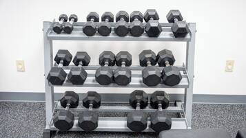 Estante metálico para mancuernas con varias filas de mancuernas hexagonales frente a una pared blanca.