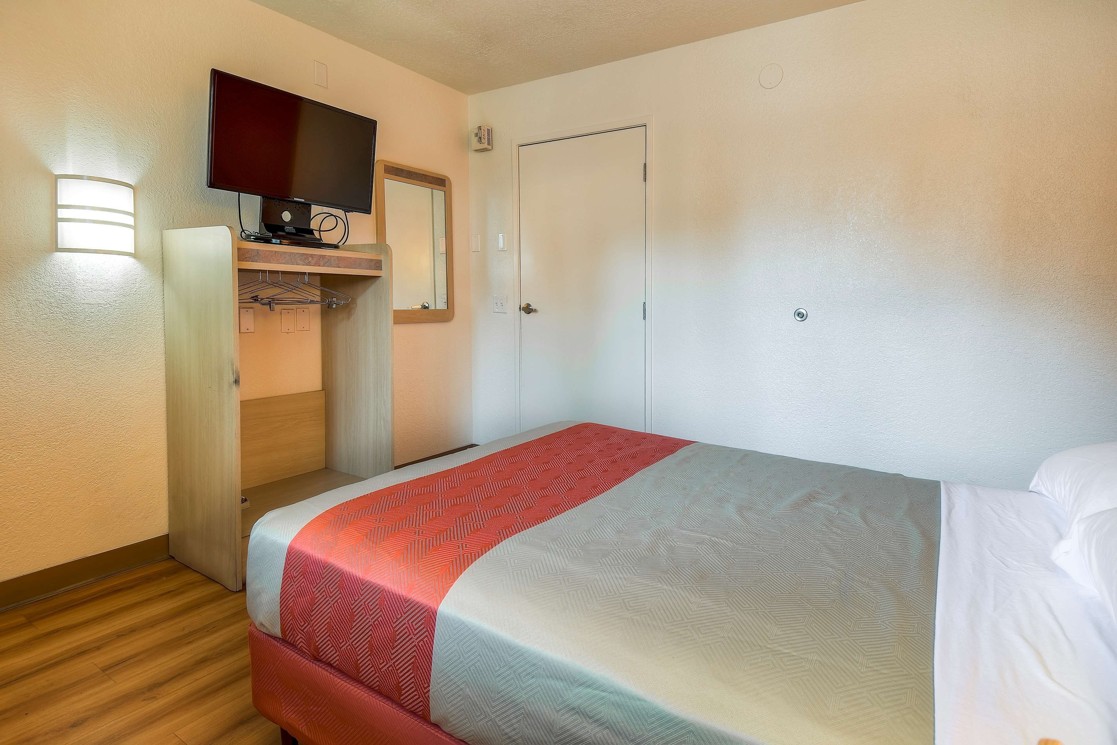 A hotel room with a bed, a television mounted on a wall, a wardrobe, and a door.