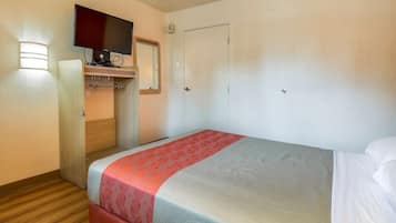 A hotel room with a bed, a television mounted on a wall, a wardrobe, and a door.