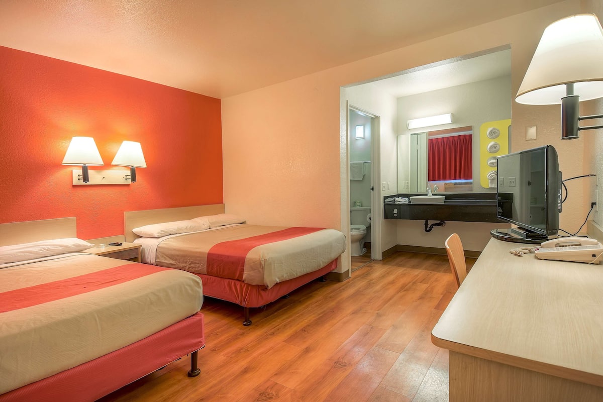 A hotel room with two beds, a desk, a television, and a bathroom visible through an open door.