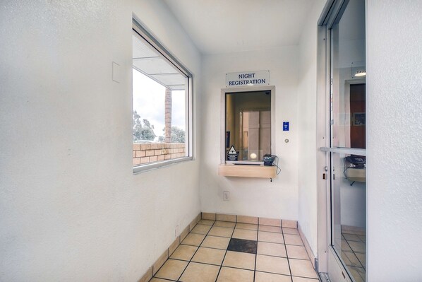 A narrow hallway with a 'Night Registration' sign, a window, and a door leading to a room. - Motel 6 Chino, CA - Los Angeles Ontario (Chino)