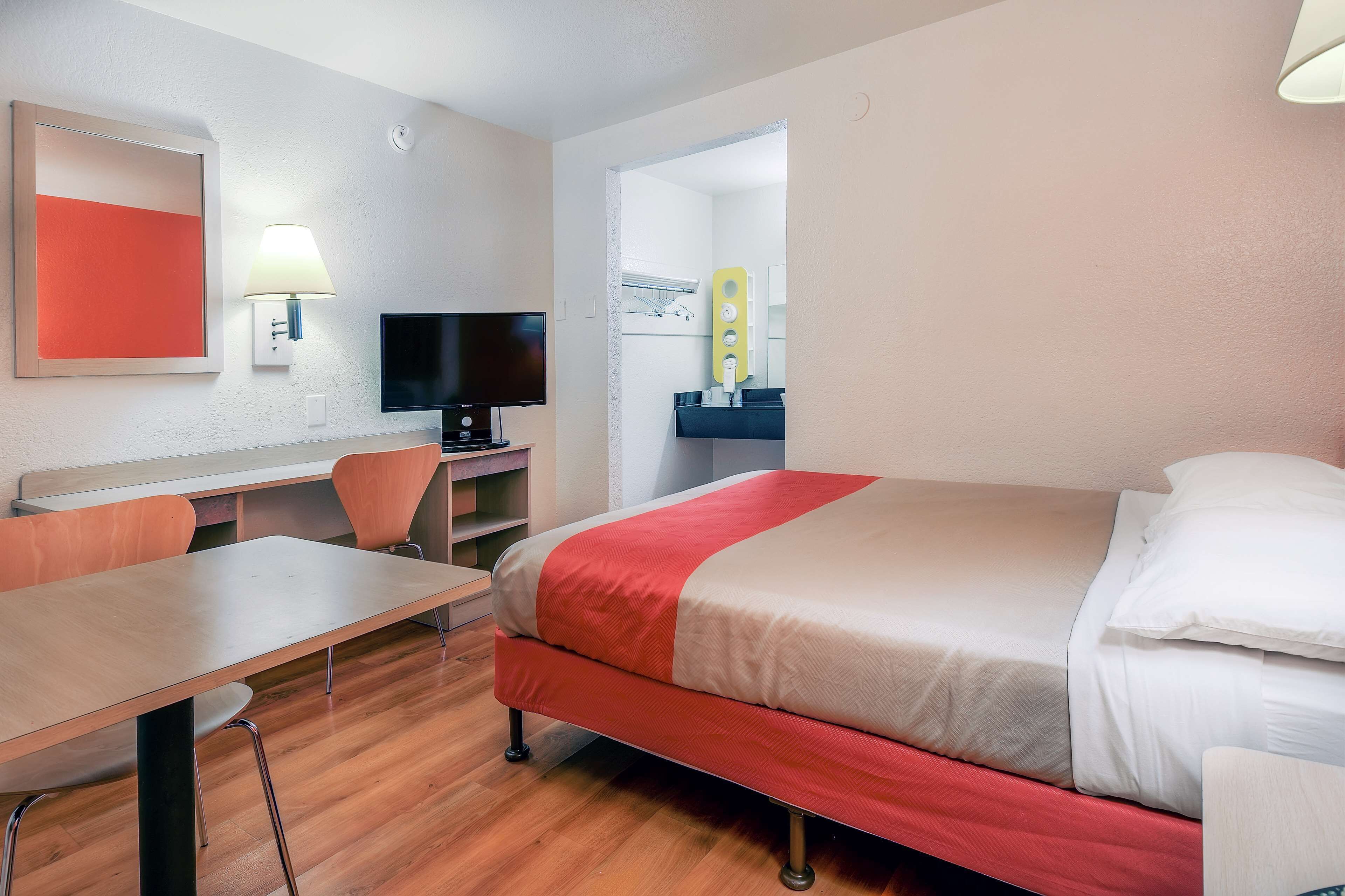A hotel room with a bed, a desk, a chair, a television, and a bathroom visible through an open door.