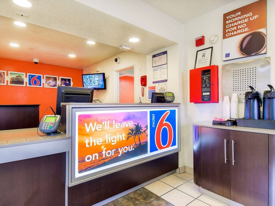 A motel reception desk with a digital screen displaying a message, a telephone, and a coffee machine.