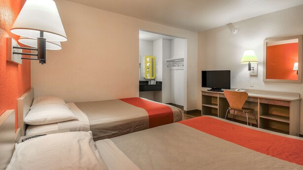 A hotel room with two single beds, a desk with a chair, a television, and a bathroom visible through an open door. - Motel 6 Chino, CA - Los Angeles Ontario (Chino)