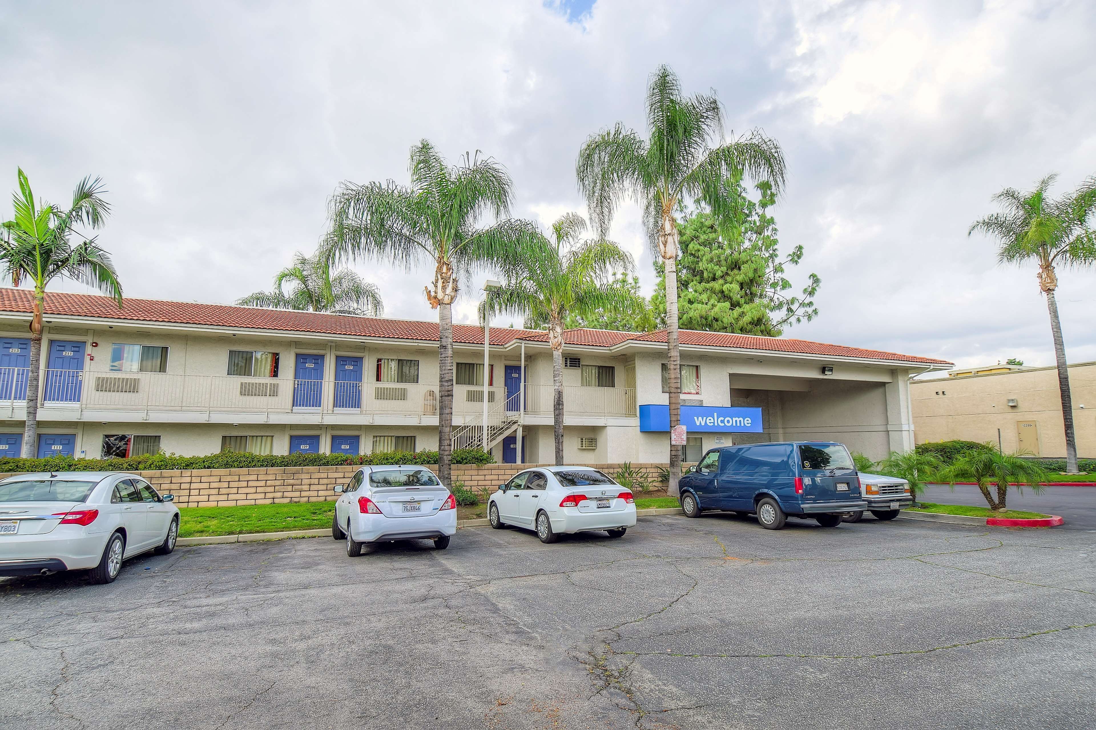 A parking lot with several cars, a building with a red-tiled roof, and palm trees.