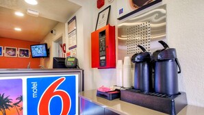 A motel reception area with a large '6' sign, a digital clock, a telephone, a red information box, and two coffee makers on the counter. - Motel 6 Chino, CA - Los Angeles Ontario (Chino)