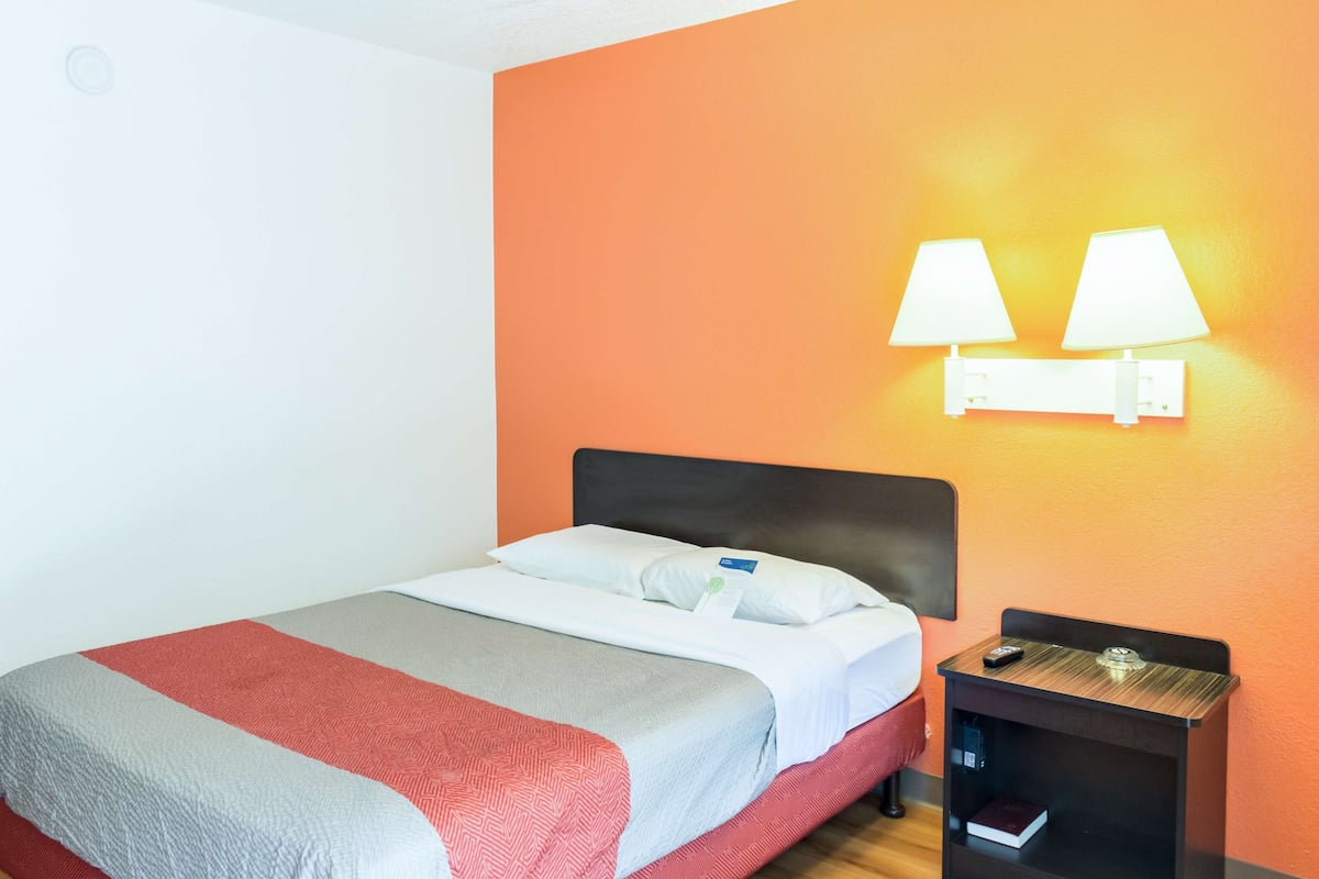 A hotel room with a bed, a nightstand, and two wall-mounted lamps.