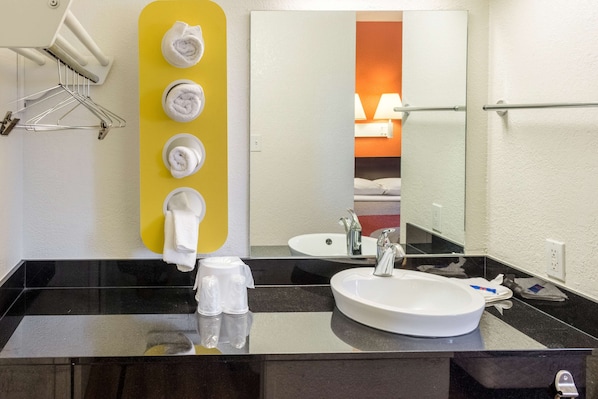 A hotel bathroom with a black countertop, a white sink, a mirror, and a yellow towel rack.