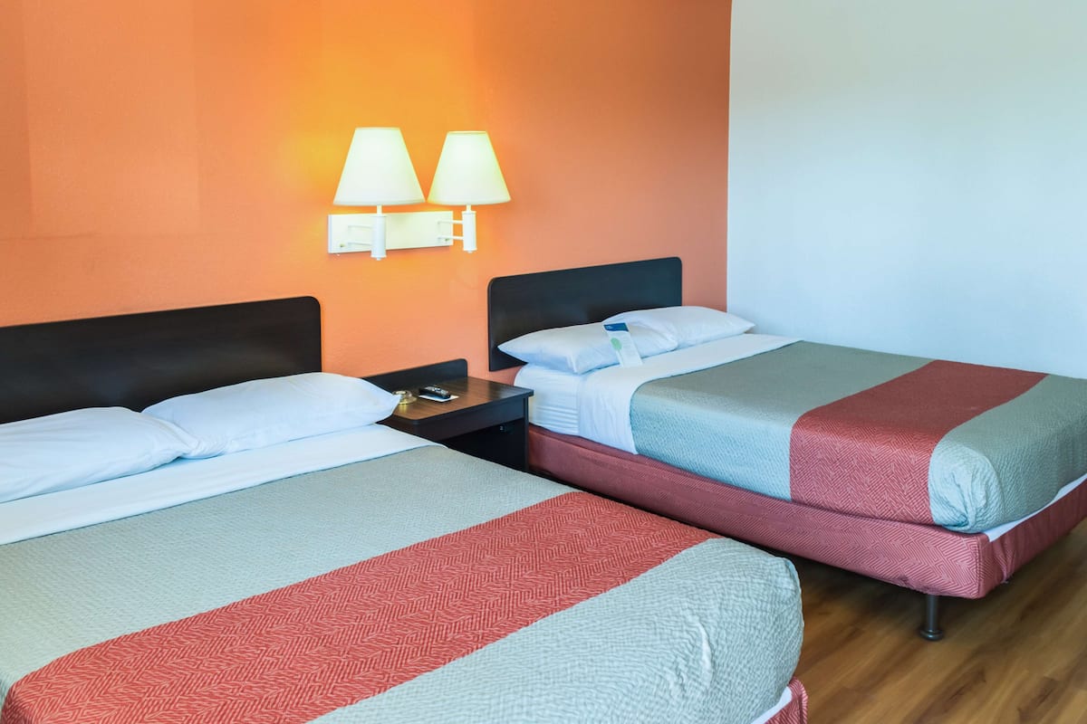 Two single beds with headboards, a nightstand with a lamp, and a wall-mounted light fixture.