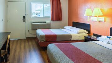 Habitación de hotel con dos camas, un escritorio, una ventana con cortinas, un equipo de aire acondicionado y lámparas fijadas a la pared.