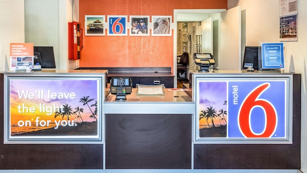 A motel reception desk with a '6' sign, a computer, and a 'We'll leave the light on for you' sign.