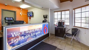 A motel reception desk with a large sign, a television, a coffee machine, and a chair. - Motel 6 Mesa, AZ - South (Mesa)