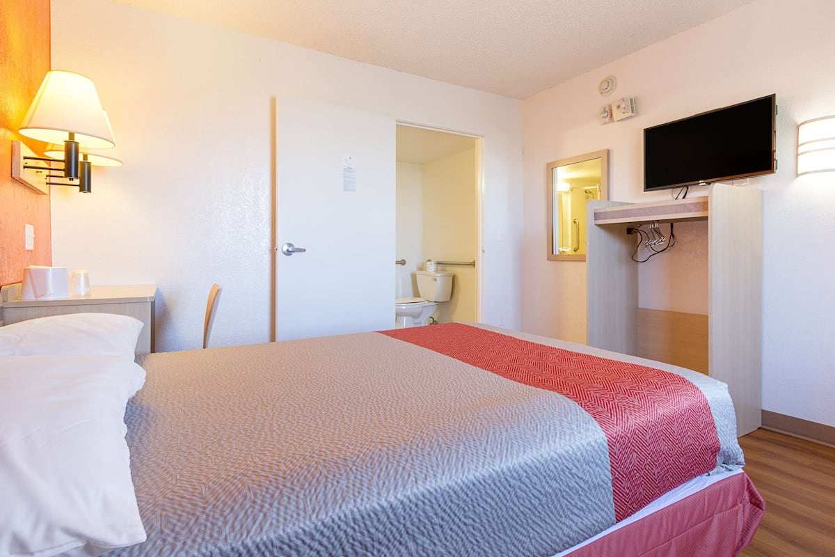 Camera d'albergo con due letti, televisione, specchio e bagno visibile attraverso una porta aperta.