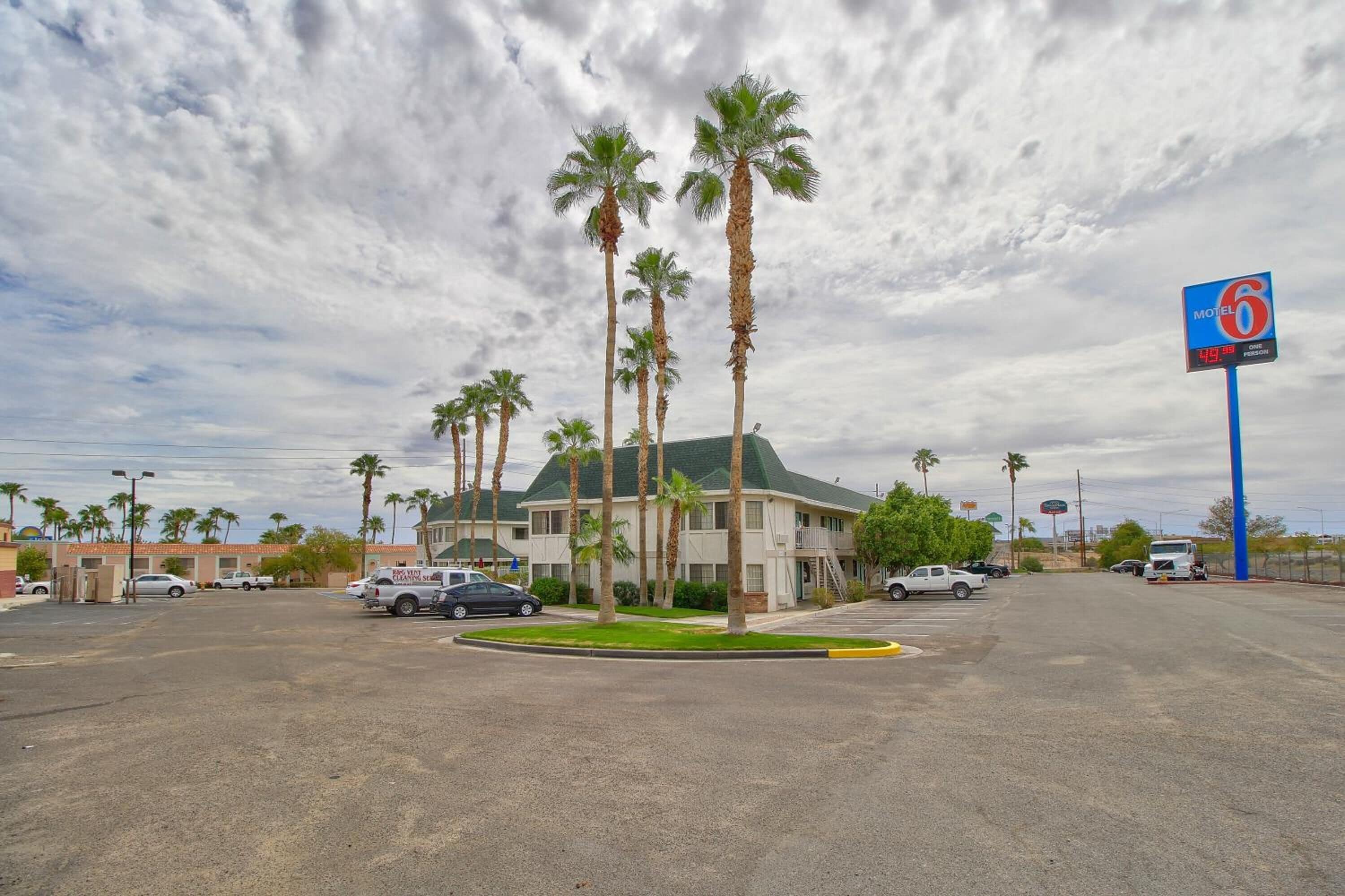 A motel with a green roof, palm trees, and a sign indicating a one-bedroom rate of $49.