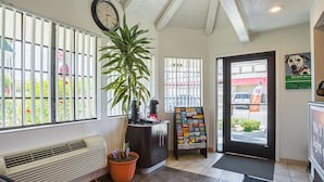 A reception area with a clock, a potted plant, a coffee machine, a bulletin board, and a door leading outside. - Motel 6 Yuma, AZ - East (Yuma)