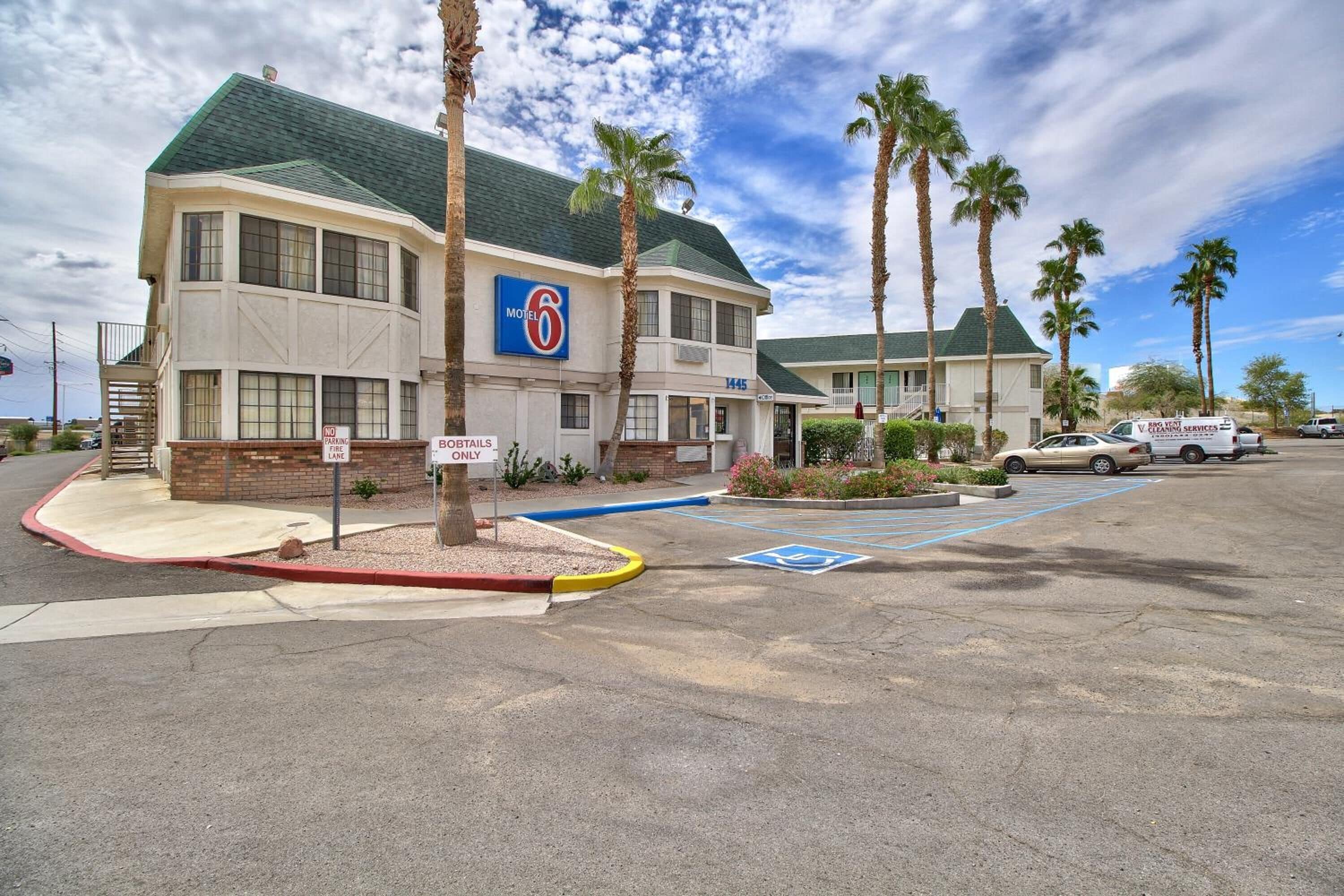 A motel with a '6' sign, parking spaces, and palm trees.