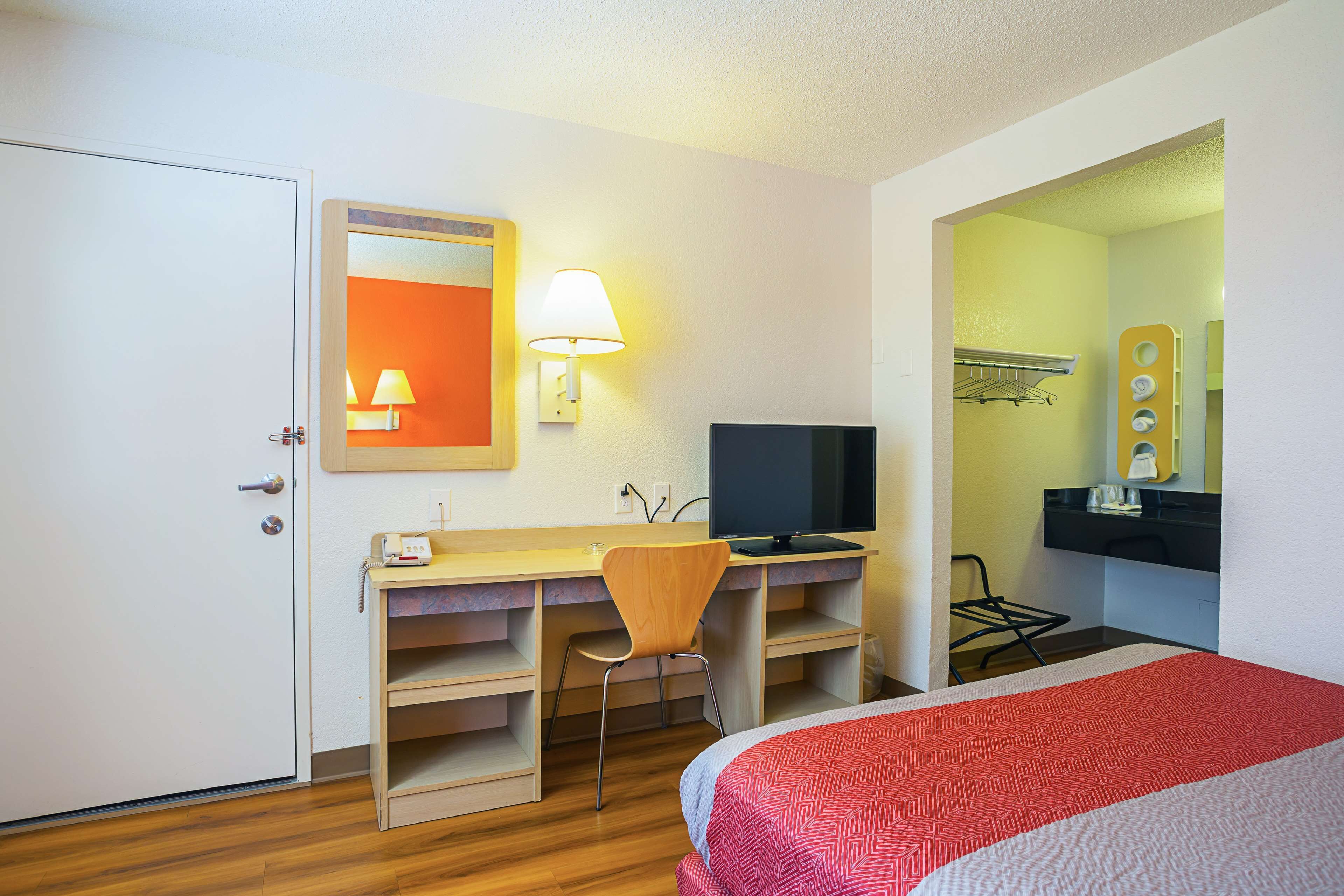 A hotel room with a bed, a desk with a chair, a television, a lamp, and a mirror.