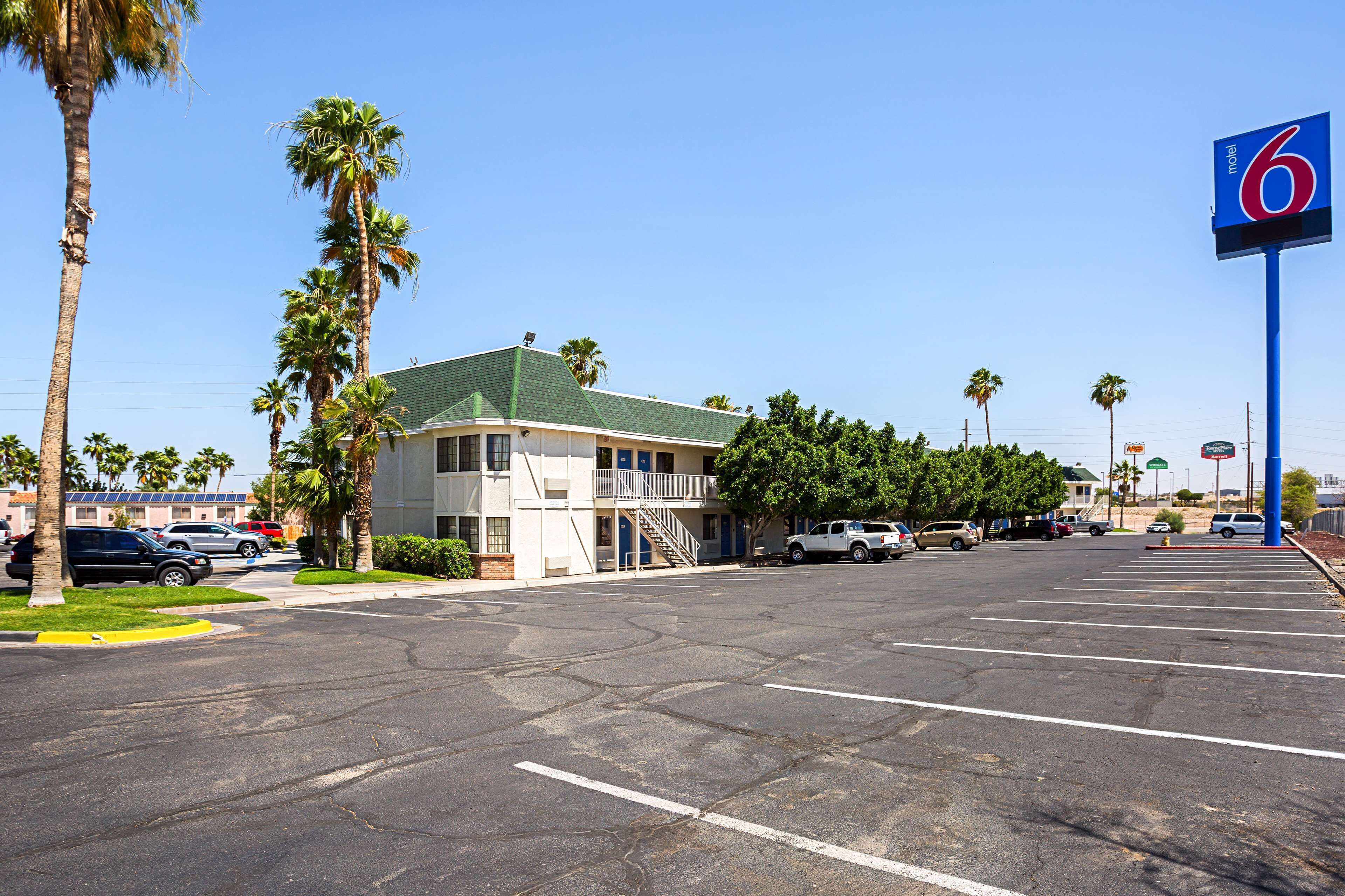 A motel with a green roof, a parking lot, and palm trees.