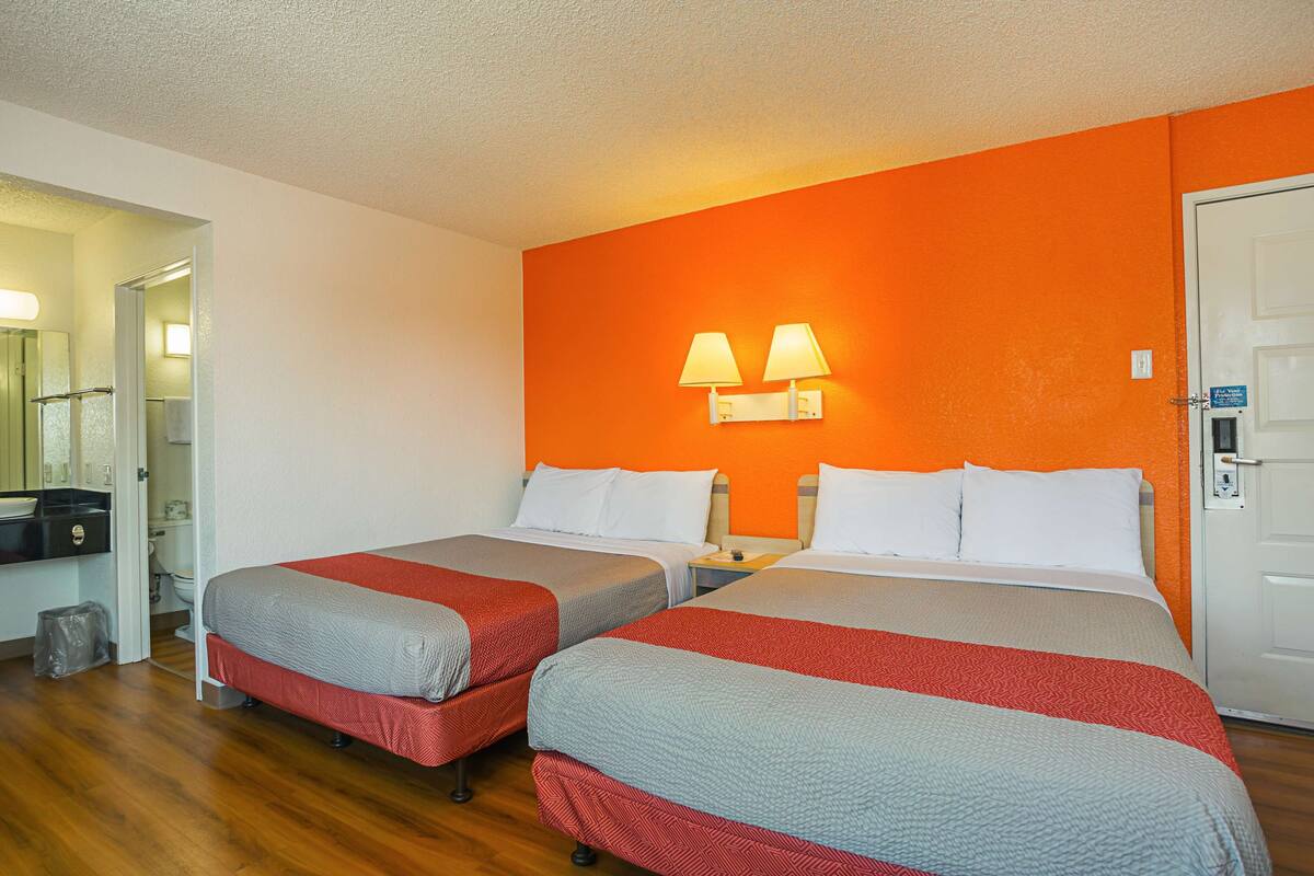 A hotel room with two beds, a bathroom, and a small kitchenette.