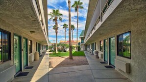 A corridor with a central pathway flanked by palm trees and a building with a textured facade. - Motel 6 Yuma, AZ - East (Yuma)