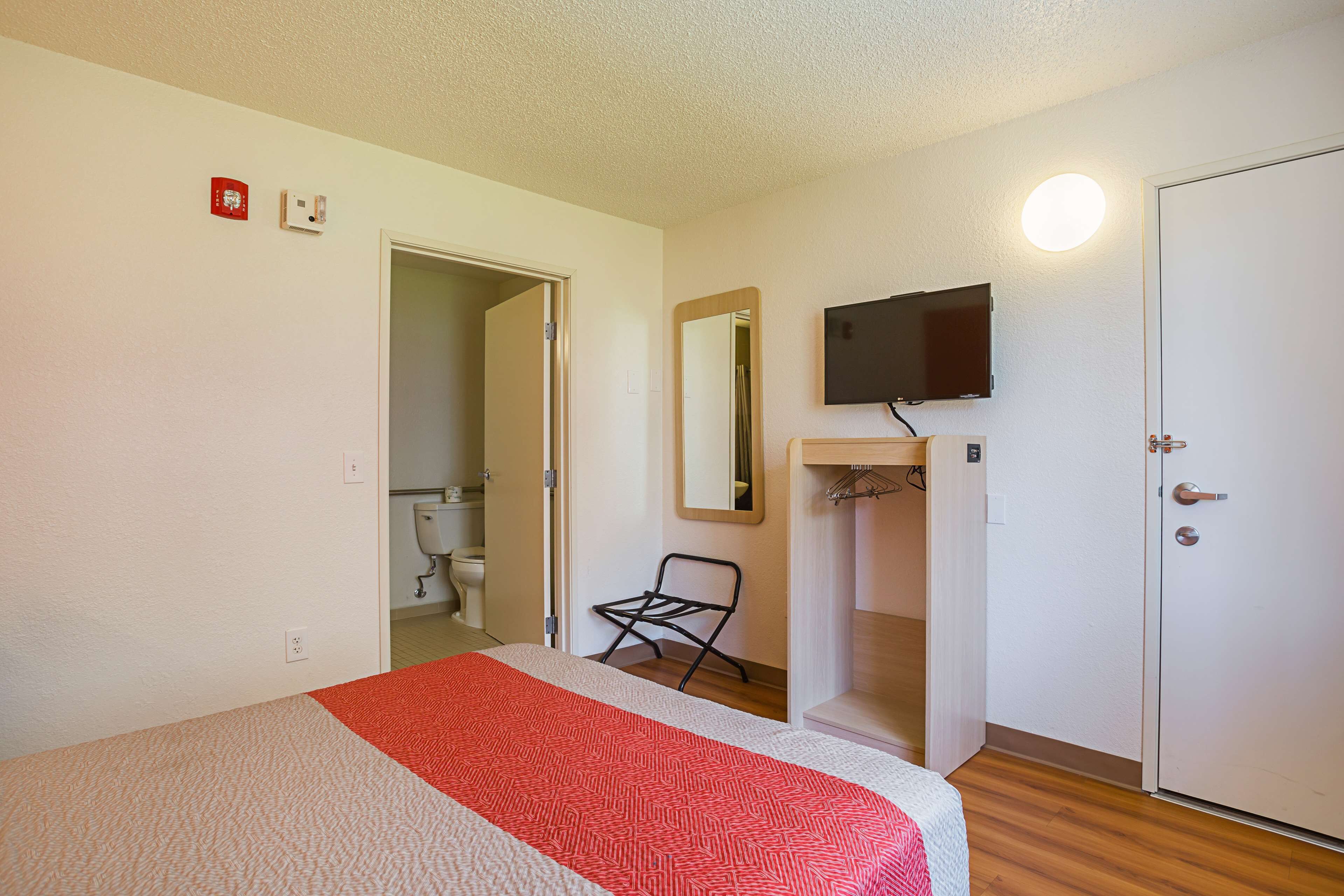 A bedroom with a bed, a TV mounted on the wall, a door, and a mirror.