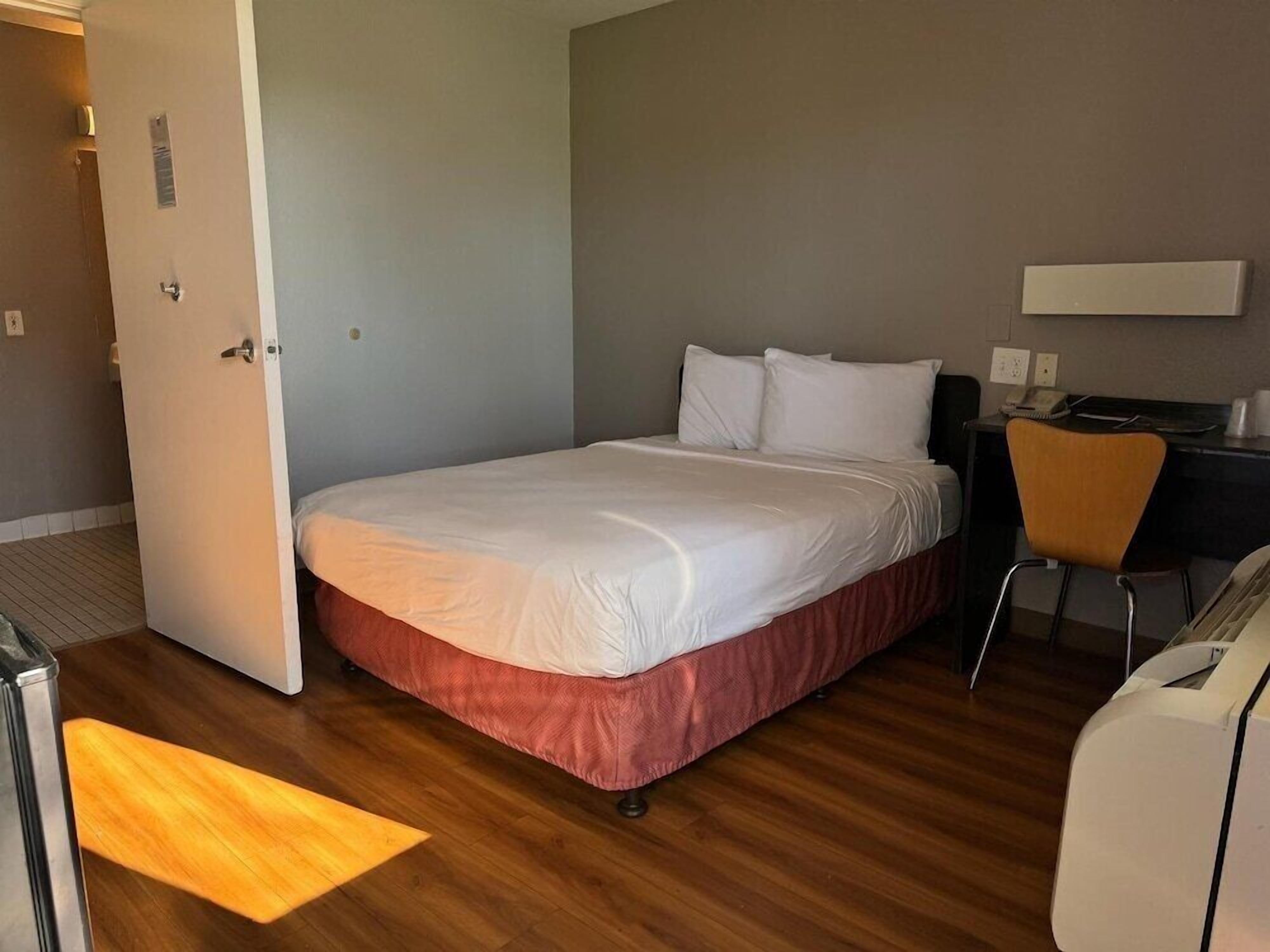 A hotel room with a bed, a desk, a chair, and a desk lamp.