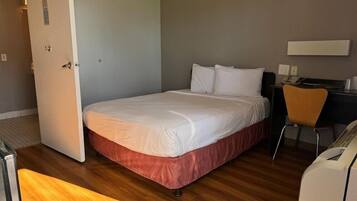 A hotel room with a bed, a desk, a chair, and a desk lamp.
