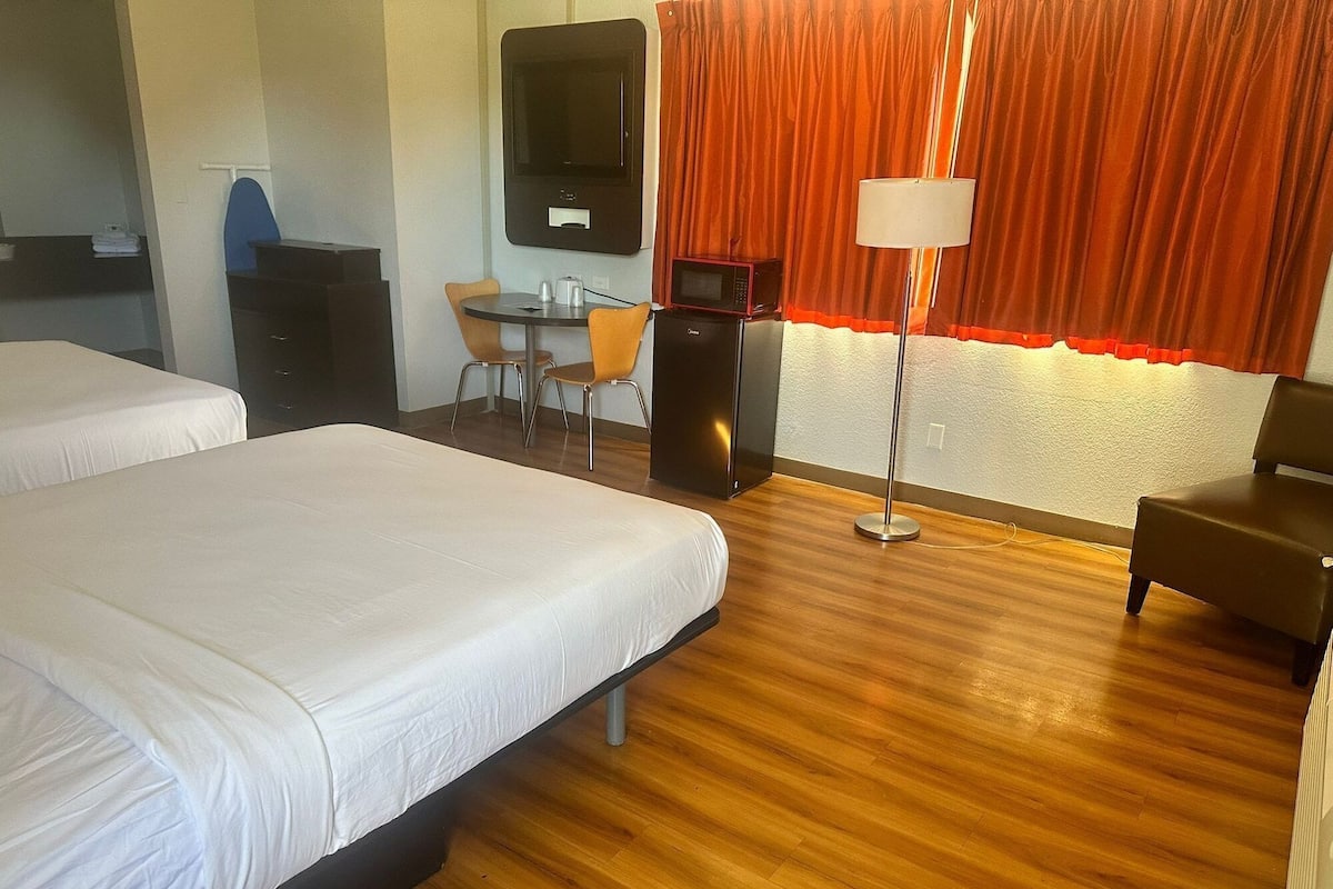 Een hotelkamer met twee bedden, een bureau, een stoel, een televisie en een lamp.