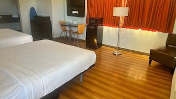 A hotel room with two beds, a desk, a chair, a television, and a lamp.