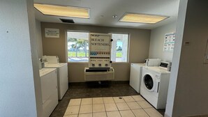 Une buanderie équipée d’un lave-linge, d’un sèche-linge et d’un panneau indiquant l’emplacement du savon, de l’eau de Javel et de l’adoucissant.