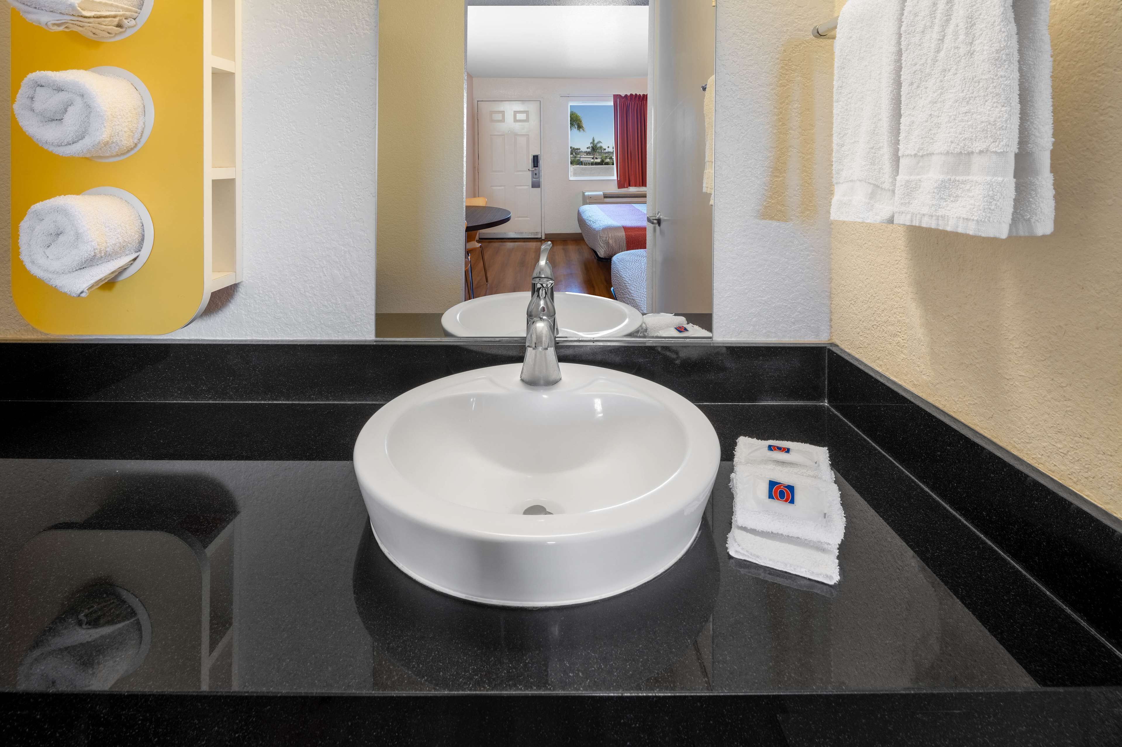 Un baño con un lavamanos redondo, un espejo y un toallero amarillo.