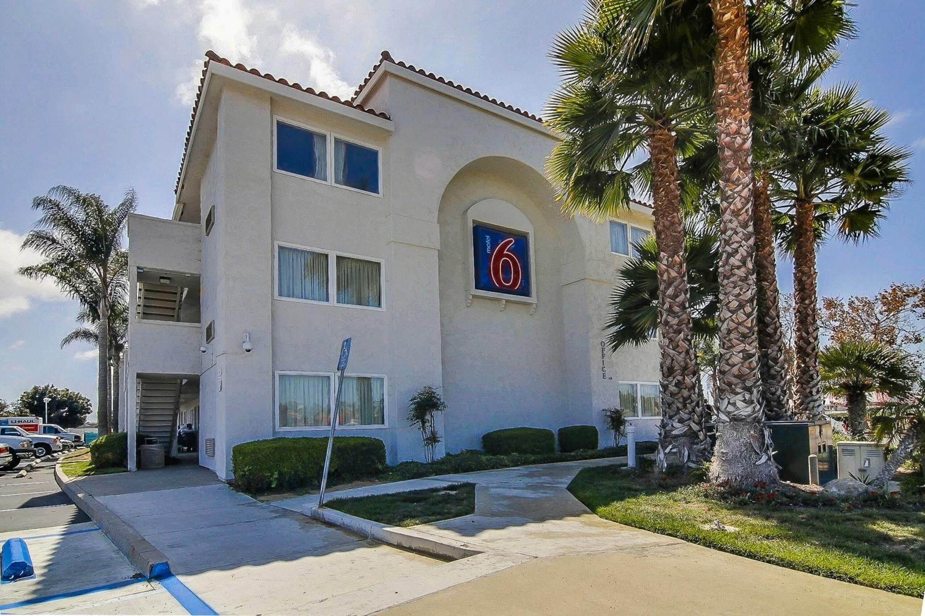 A two-story motel with a '6' sign, palm trees, and a parking lot.