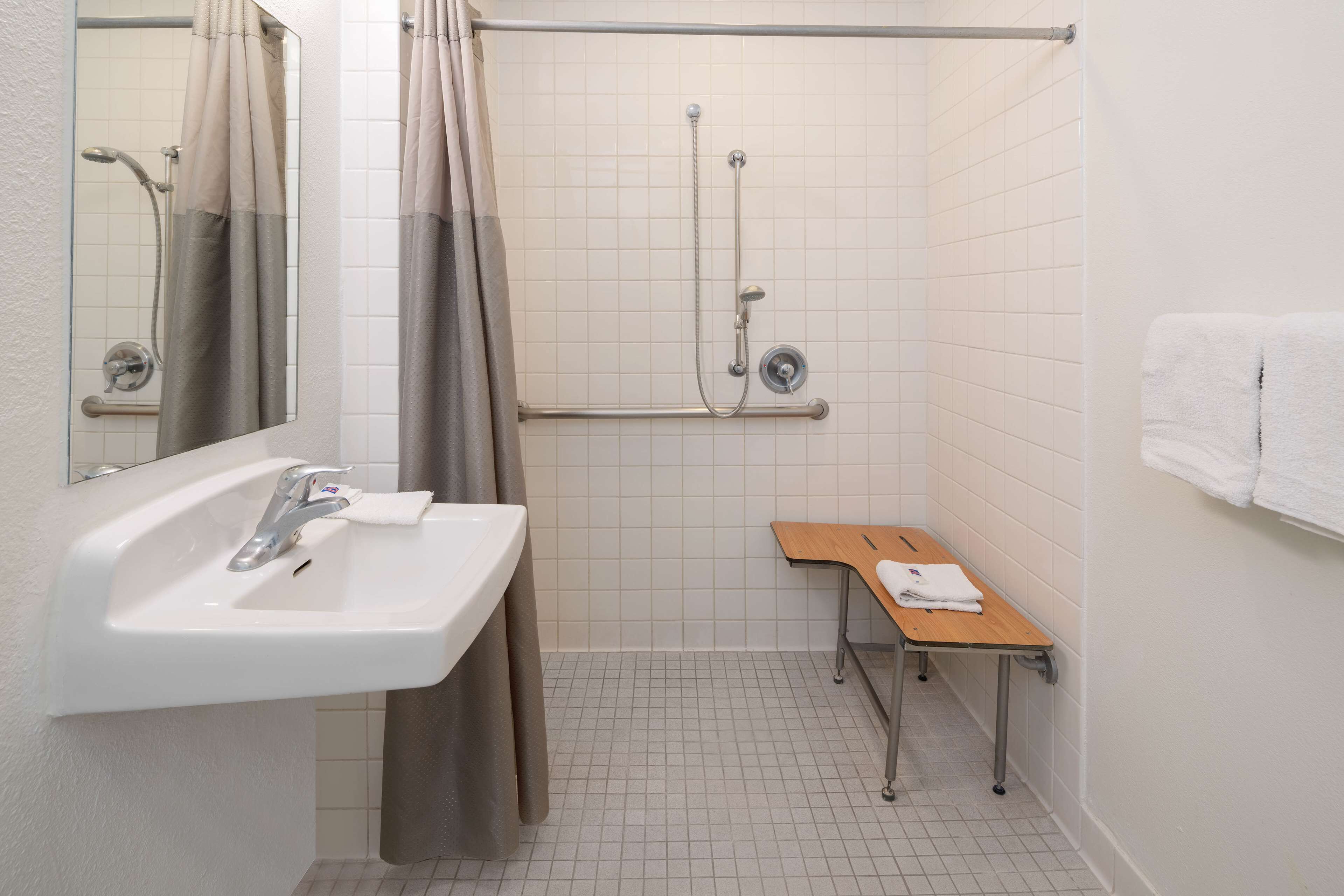 A bathroom with a sink, mirror, shower, and a bench with towels.